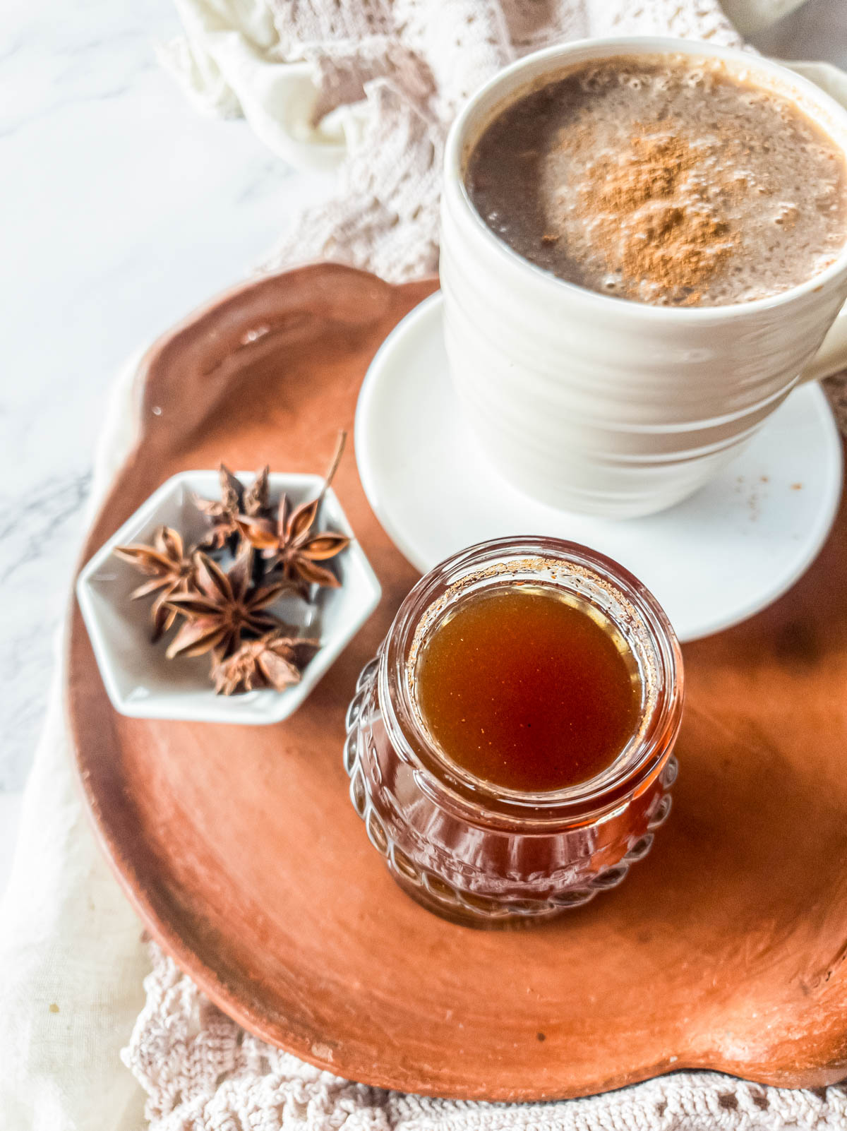 Terra cotta tray with latte in white mug with saucer and simple syrup in glass jar.