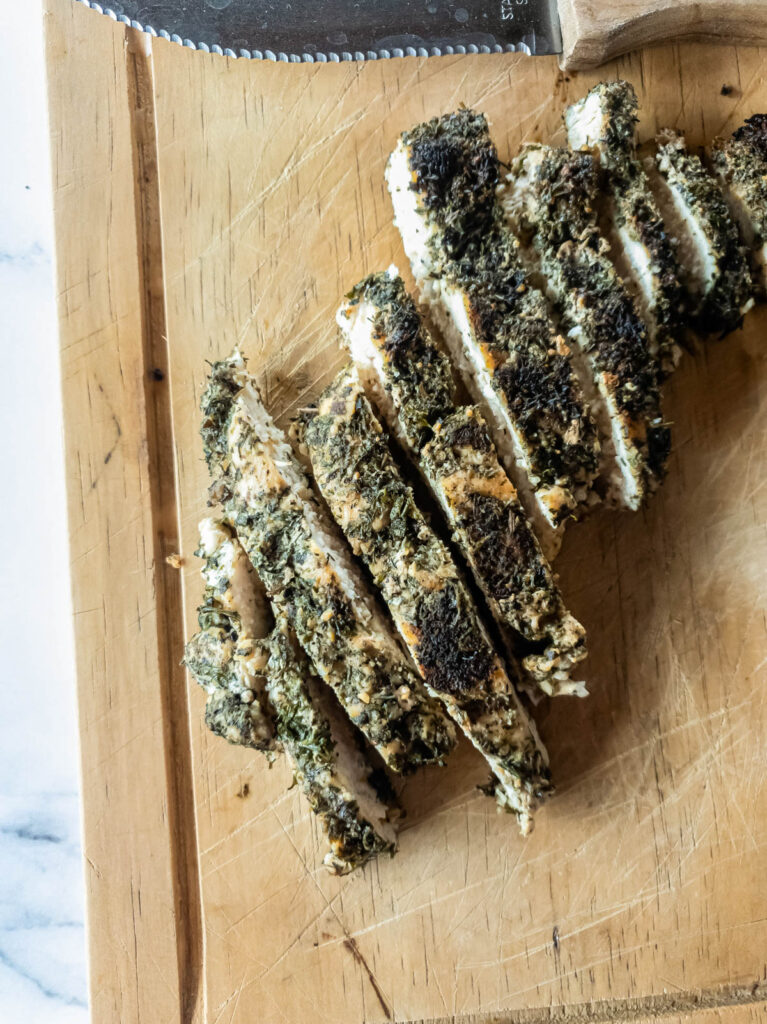 A picture of cooked herb chicken on wood cutting board, sliced in strips.