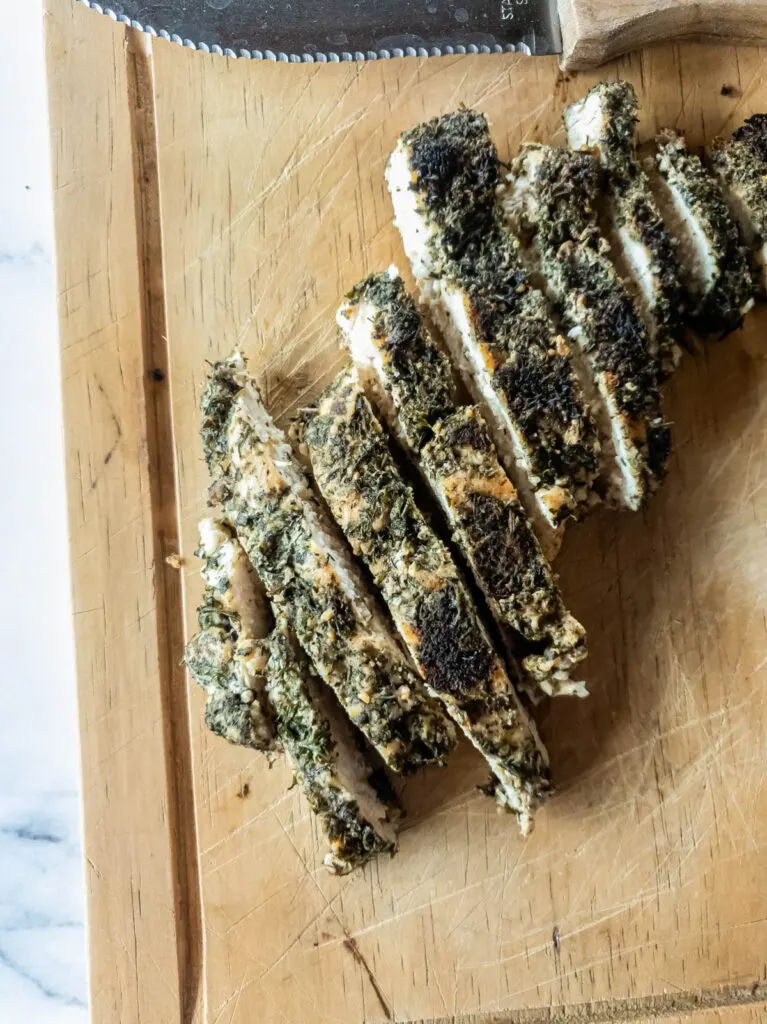 Cooked herb chicken on wood cutting board, sliced in strips.