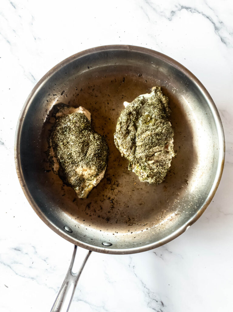 Two chicken breasts cooking in skillet.