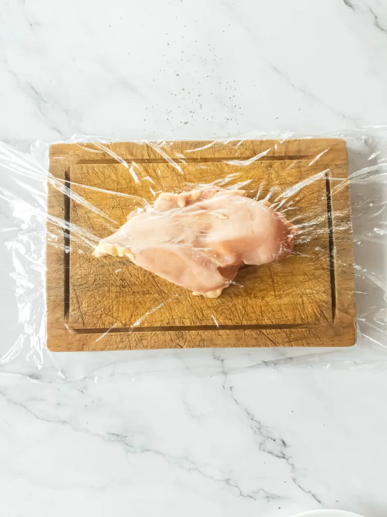 A picture of chicken breast under a layer of plastic wrap.