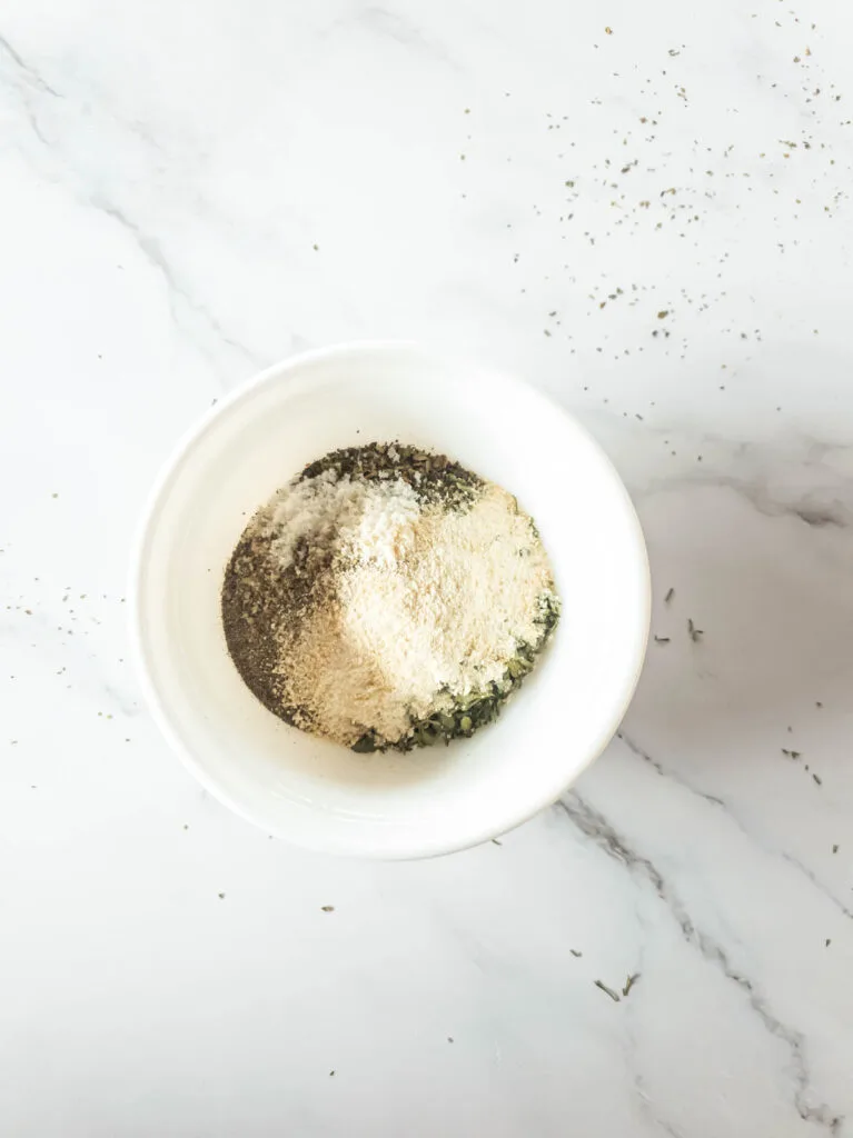 A picture of herbs and salt in white bowl for coating chicken.