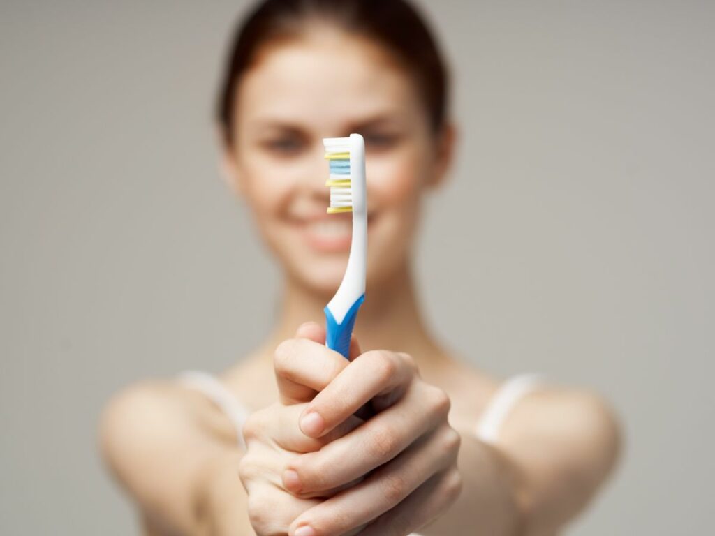 A woman holding toothbrush straight in front of her with two hands.