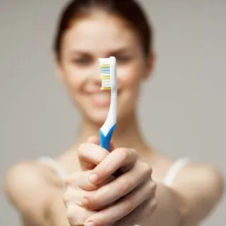 A young woman holding blue and white toothbrush with blurred body.