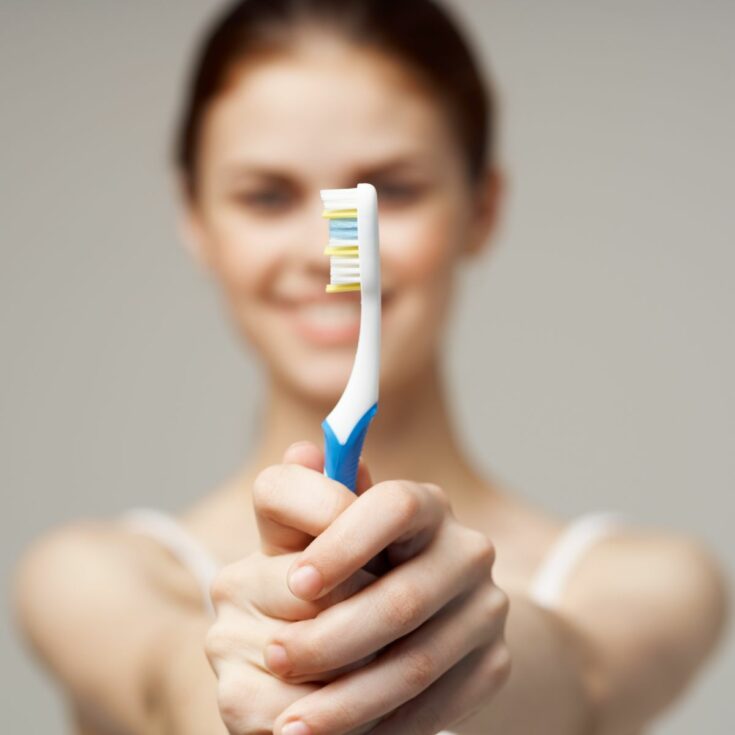 Pretty young woman holding blue and white toothbrush with blurred body.