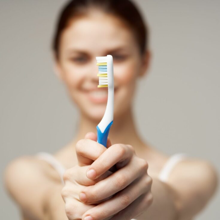 A young woman holding blue and white toothbrush with blurred body.