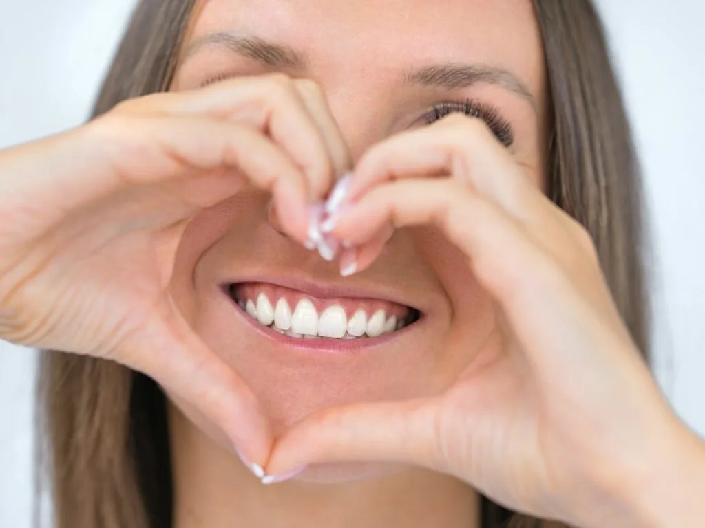 Woman smiling with hands in shape of a heart over her face.