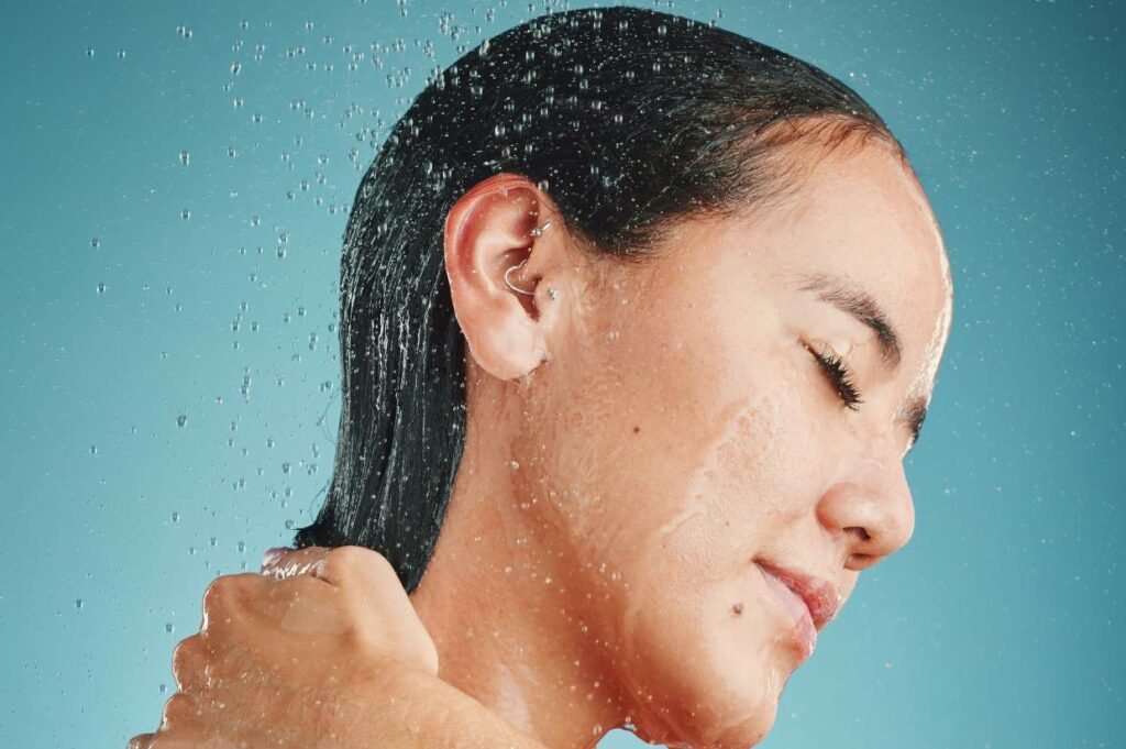 A woman is showering with water falling on hair and ears.