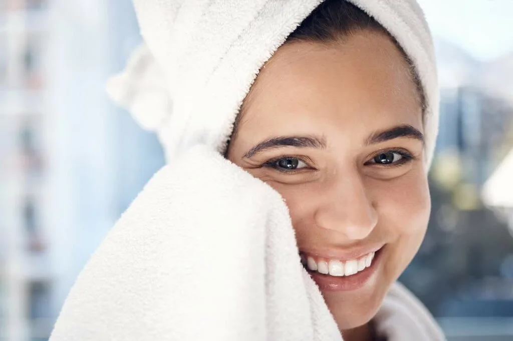 A smiling woman with a towel wrapped around her head drying off her face.