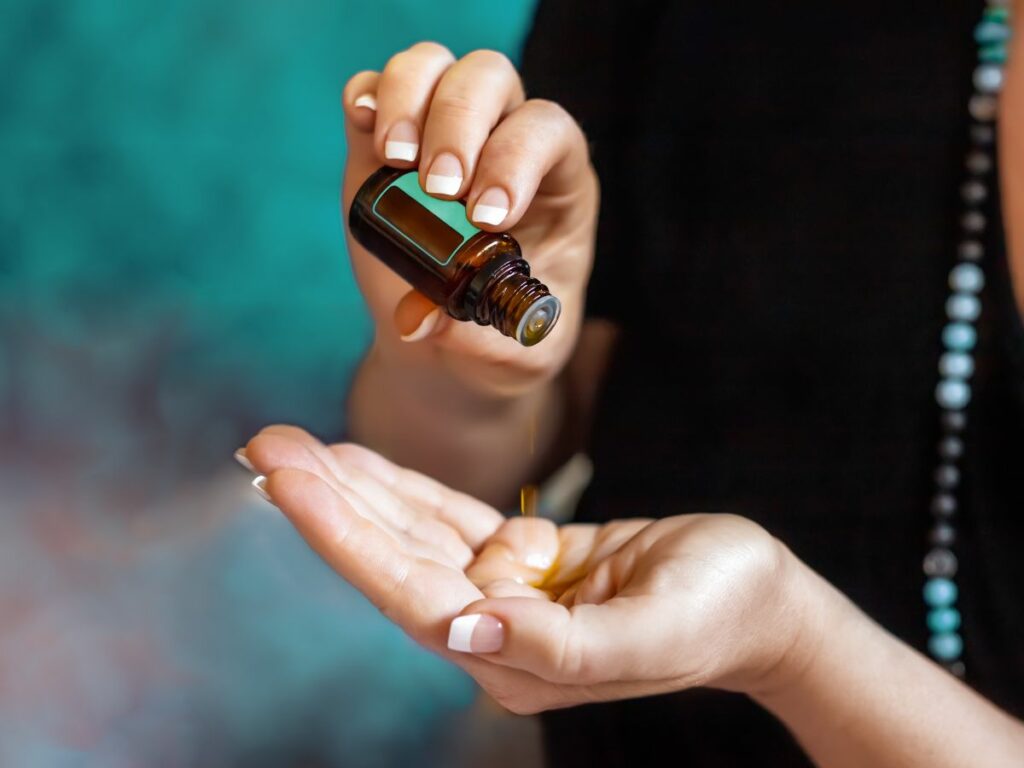 A woman applying essential oil from bottle to open hand.