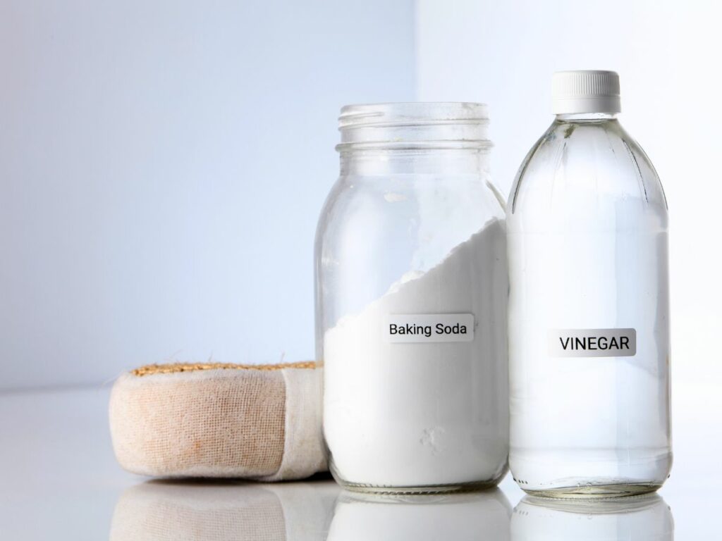 Bottles of white vinegar and baking soda next to a sponge.