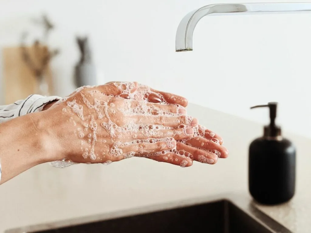 Woman washing hands at sink with bubbles.