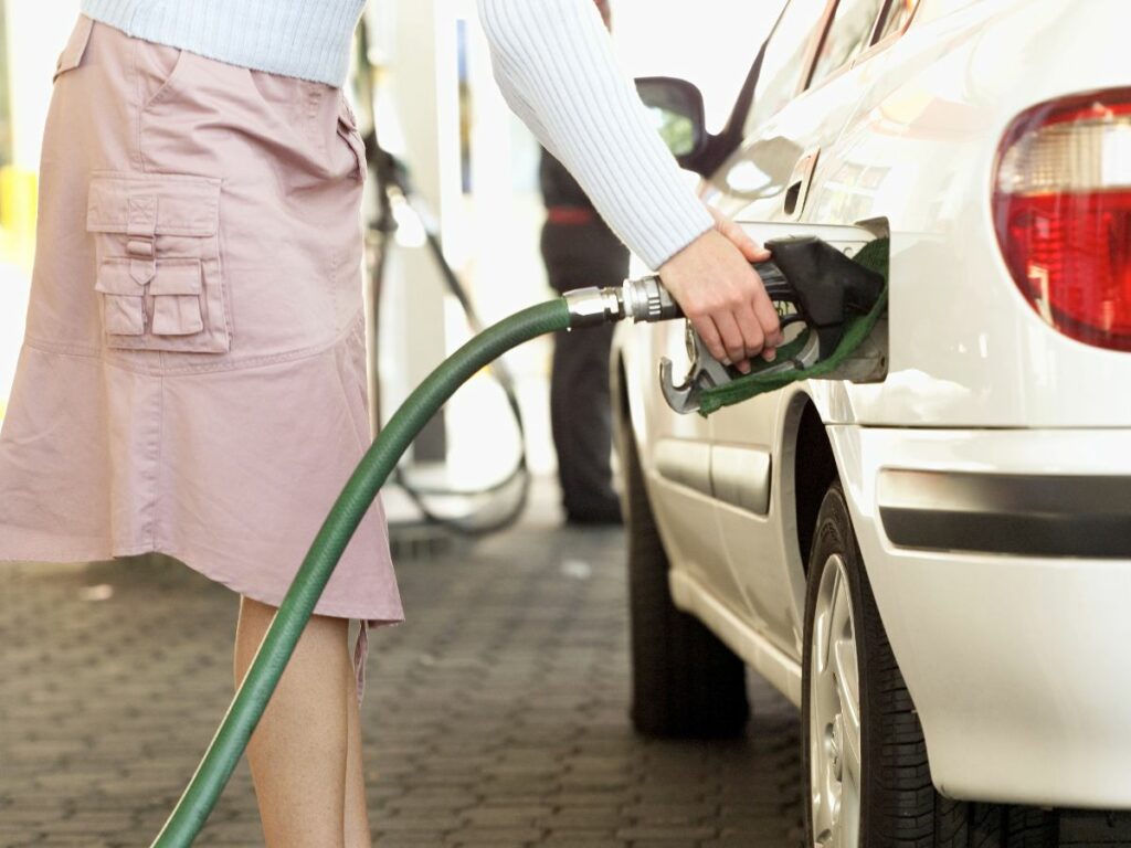 A woman pumping gas at station in pink skirt.