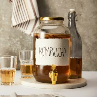 Glass jar labeled kombucha on wooden tray with towel in background.