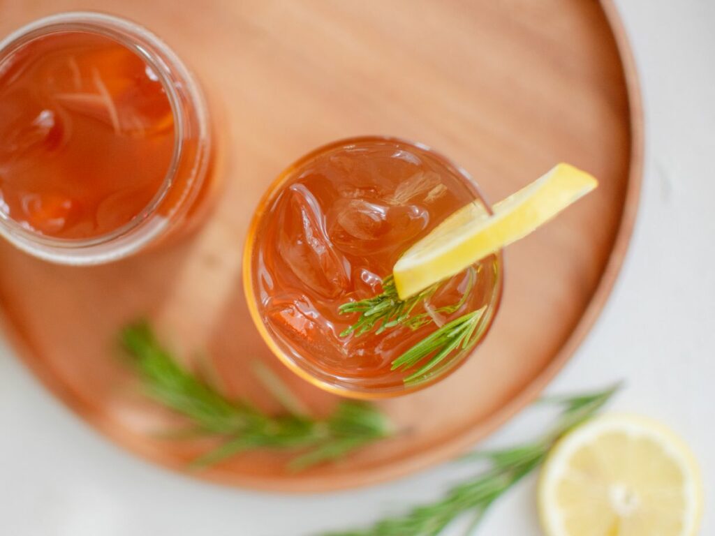 Two cups of kombucha with lemon slice and sprig of fresh rosemary.