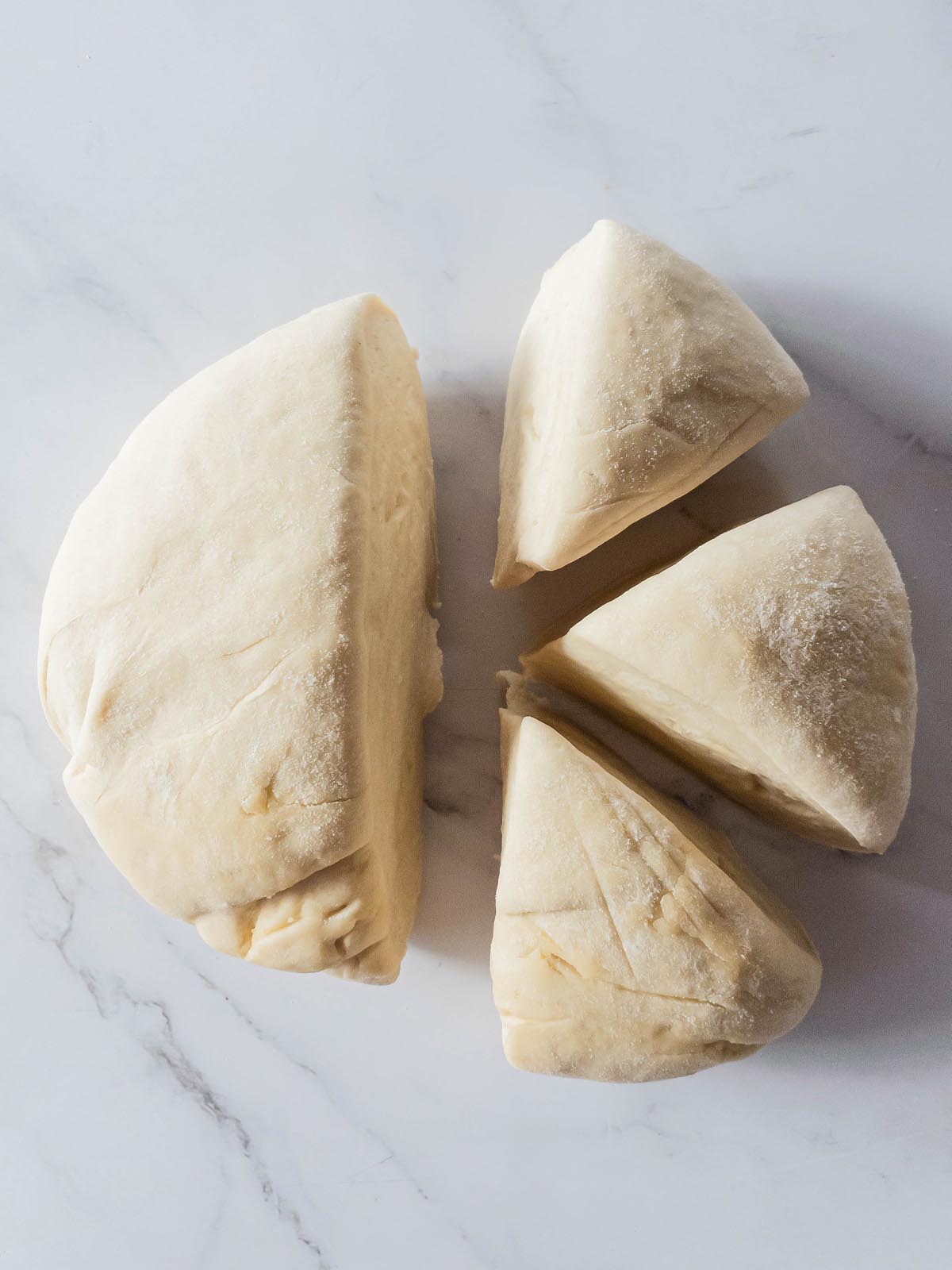 Four portions of Jimmy John's bread dough on a marble surface.