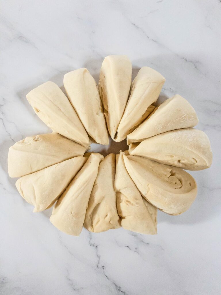 A circle of bread dough wedges on a marble surface.
