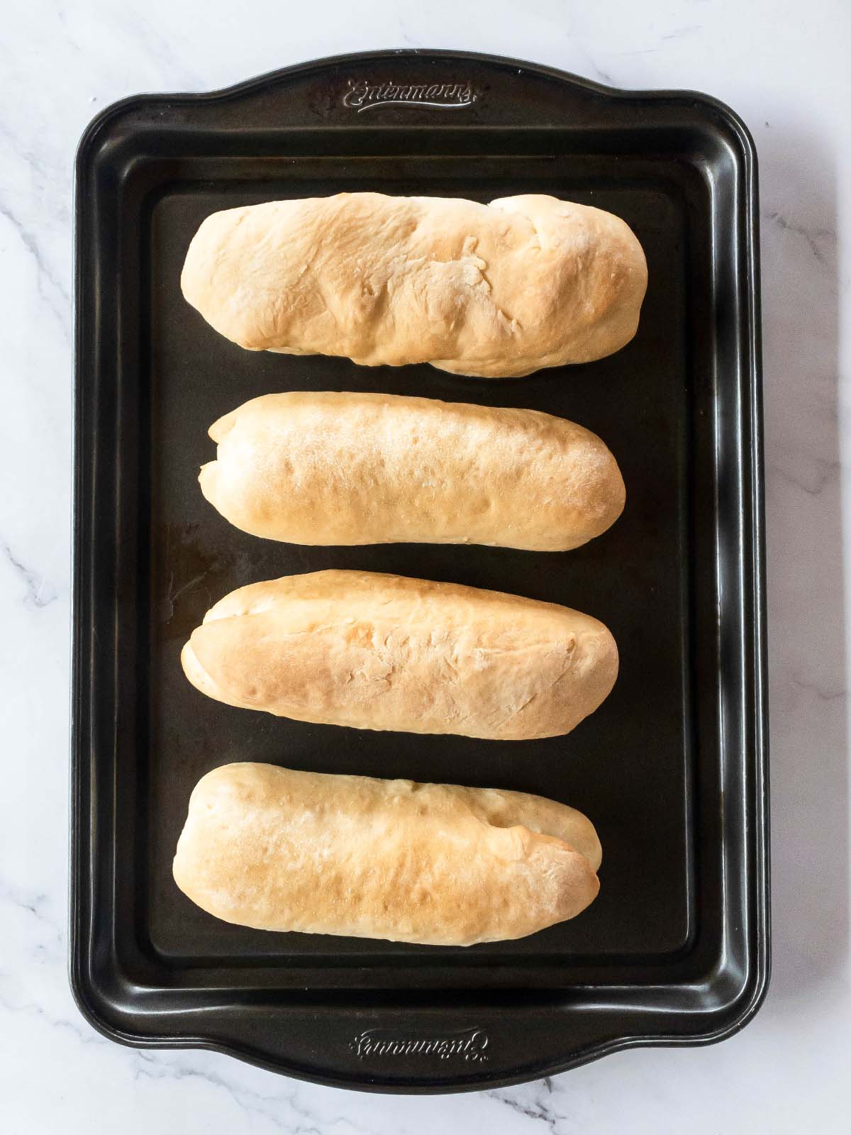 Four baked Jimmy Johns bread loafs on a baking sheet.