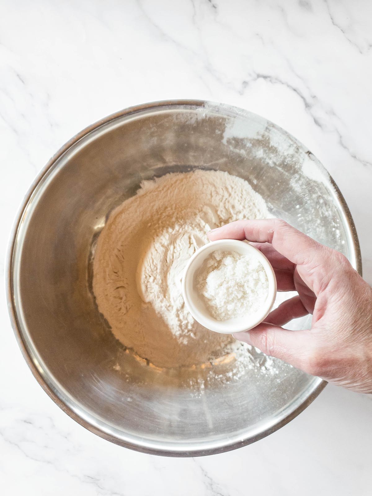 A person preparing Jimmy John's bread by pouring salt into a bowl of flour.