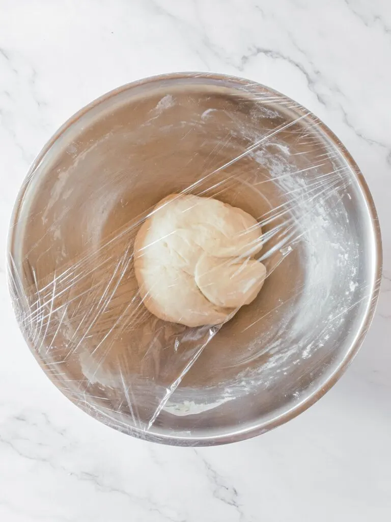 A picutre of the dough in a large bowl, covered with plastic wrap.