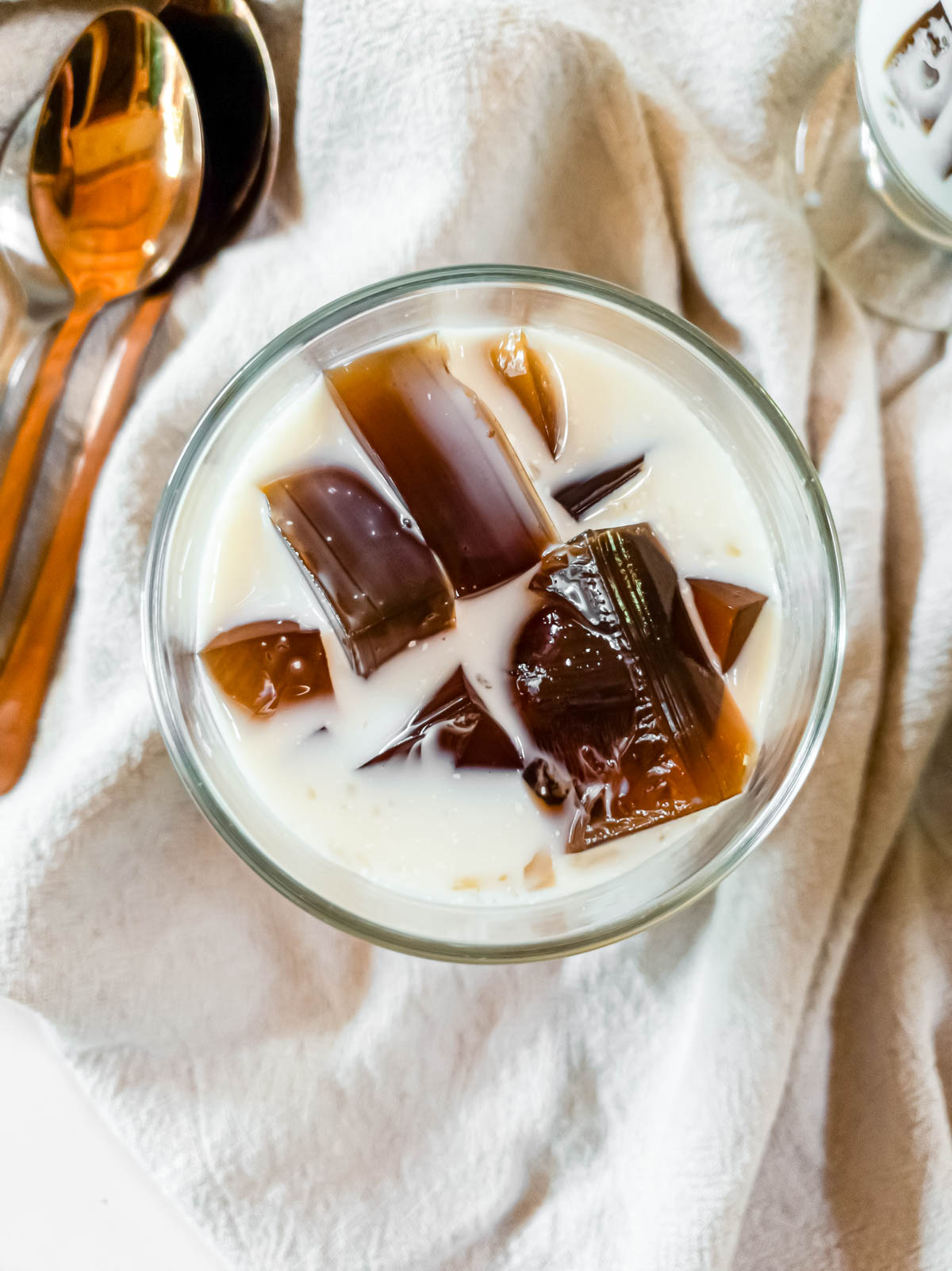 A bowl of coffee jelly with half-and-half and copper spoons.