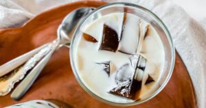 A glass with coffee jelly and multiple silver spoons next to it.