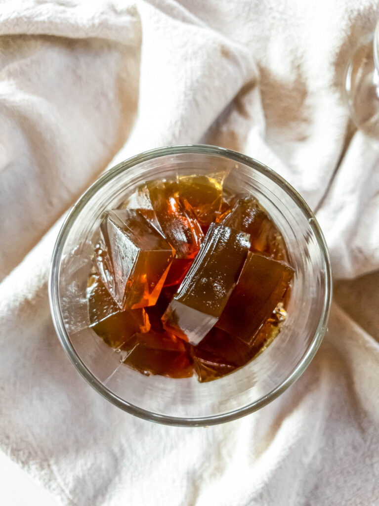 A glass of with saiki k coffee jelly cubes in it on fabric background.