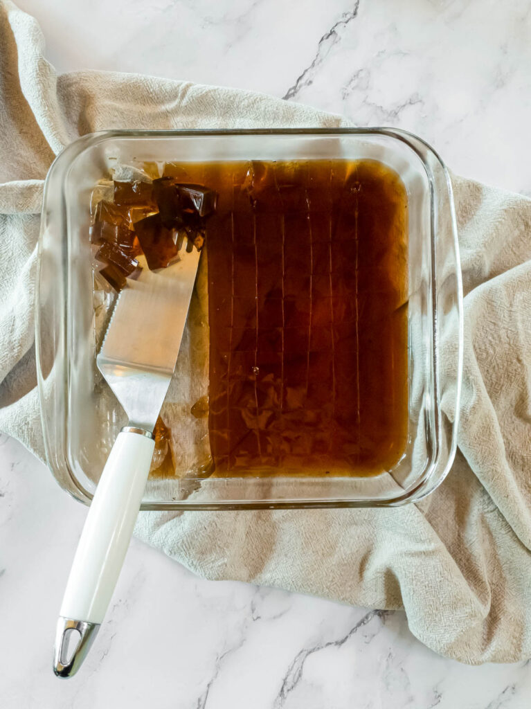 A glass dish with chilled saiki k coffee jelly and a spatula in it.