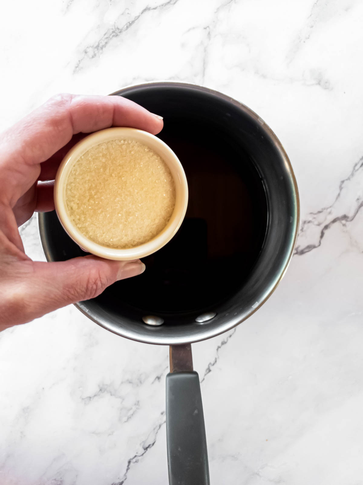 A person holding a cup sugar over a pot of coffee.