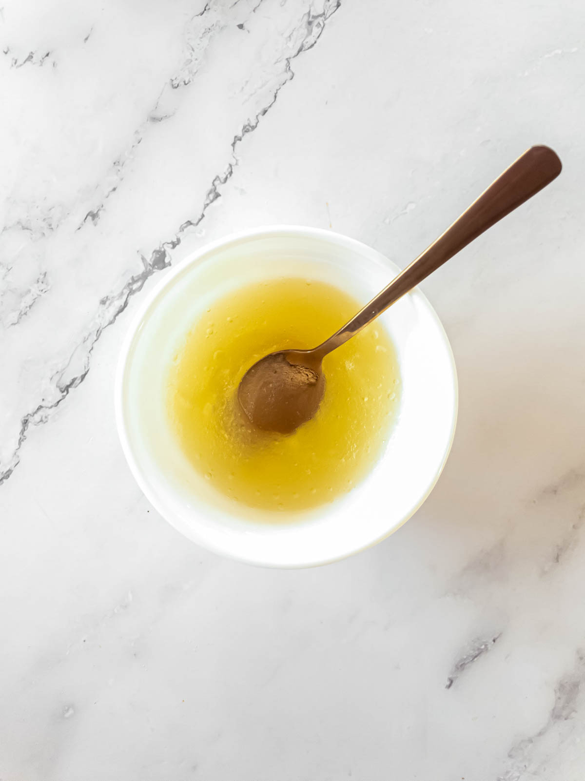 A bowl of gelatin blooming with a spoon on a marble stone.