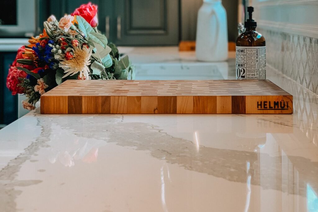 A wooden cutting board with flowers on it, clean quartz countertop in foreground.