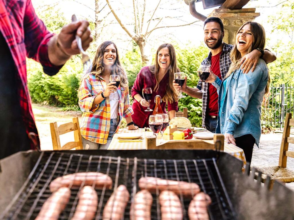 Happy friends at a backyard bbq grilling sausages.