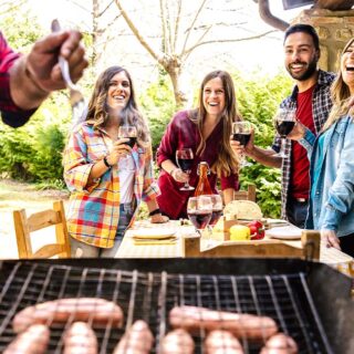 A backyard BBQ with friends grilling sausages on a grill.