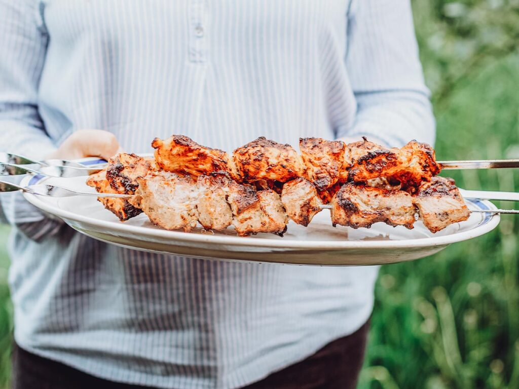 A woman grilling skewered meat at a backyard BBQ.