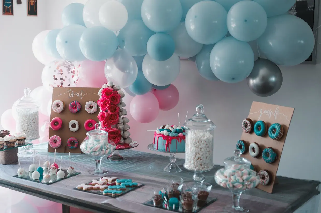 A table filled with donuts and cupcakes with balloon arch above.