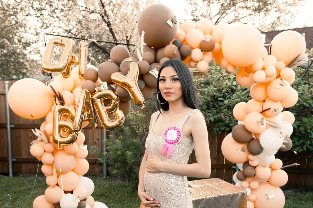 A pregnant woman posing in front of a balloon arch.