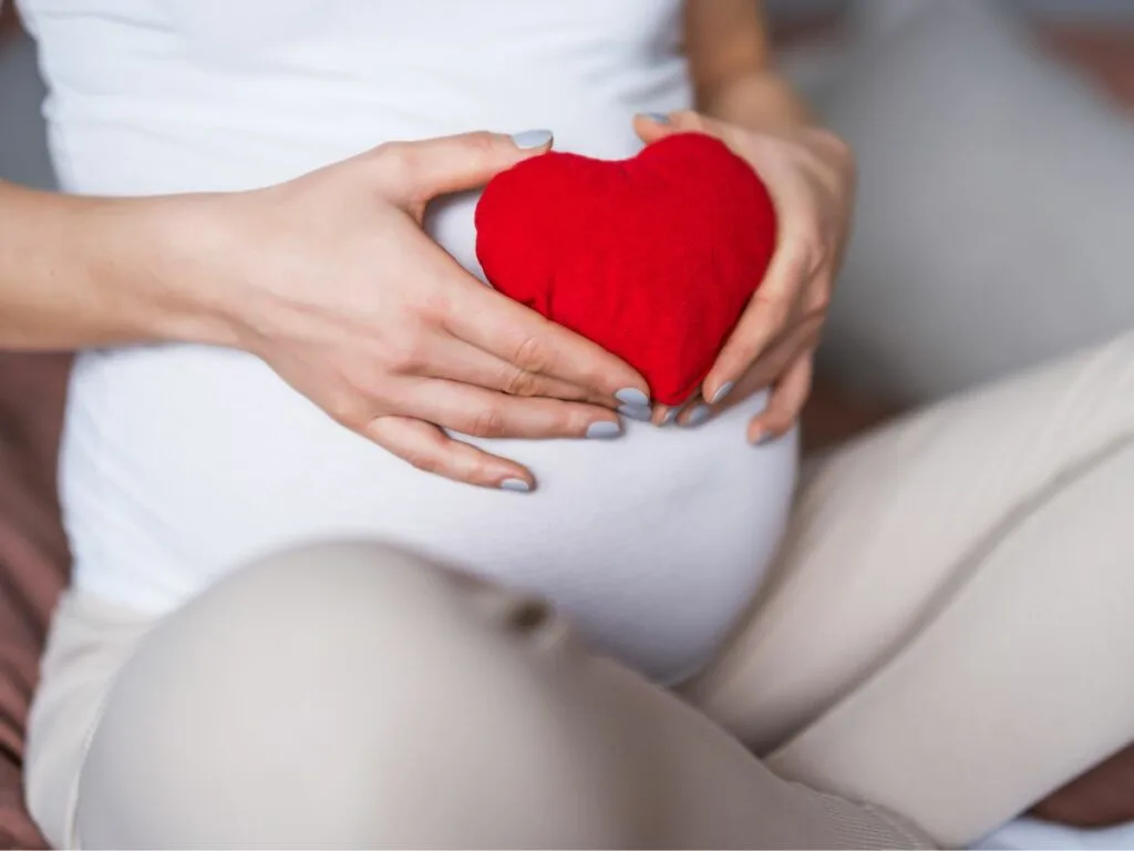 A pregnant woman holding a red heart in her hands.