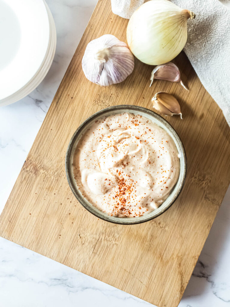 A bowl of homemade spicy mayonnaise with garlic and onions on a cutting board.