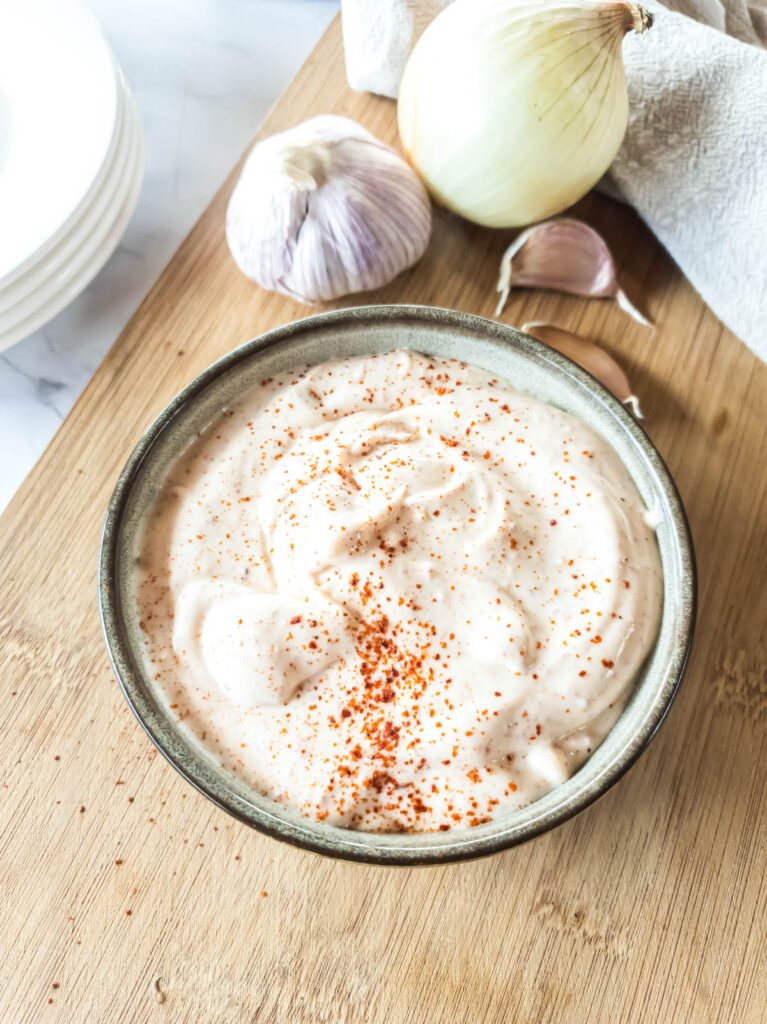 A bowl of spicy mayo garlic dip on a cutting board.