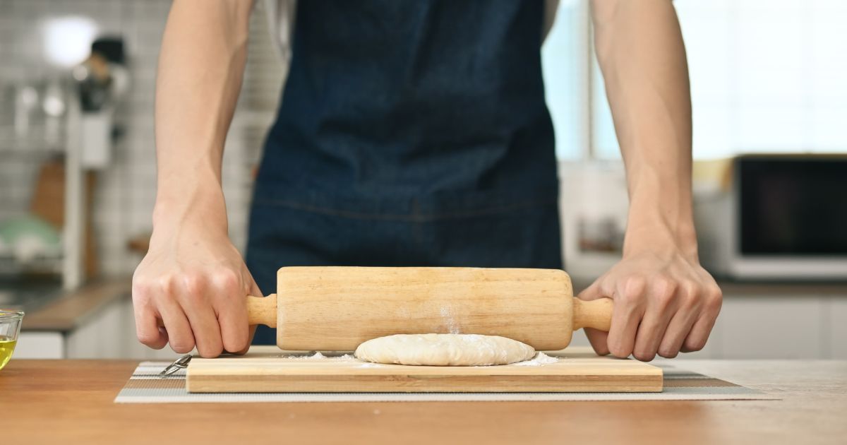 A man is rolling dough on a wooden board.