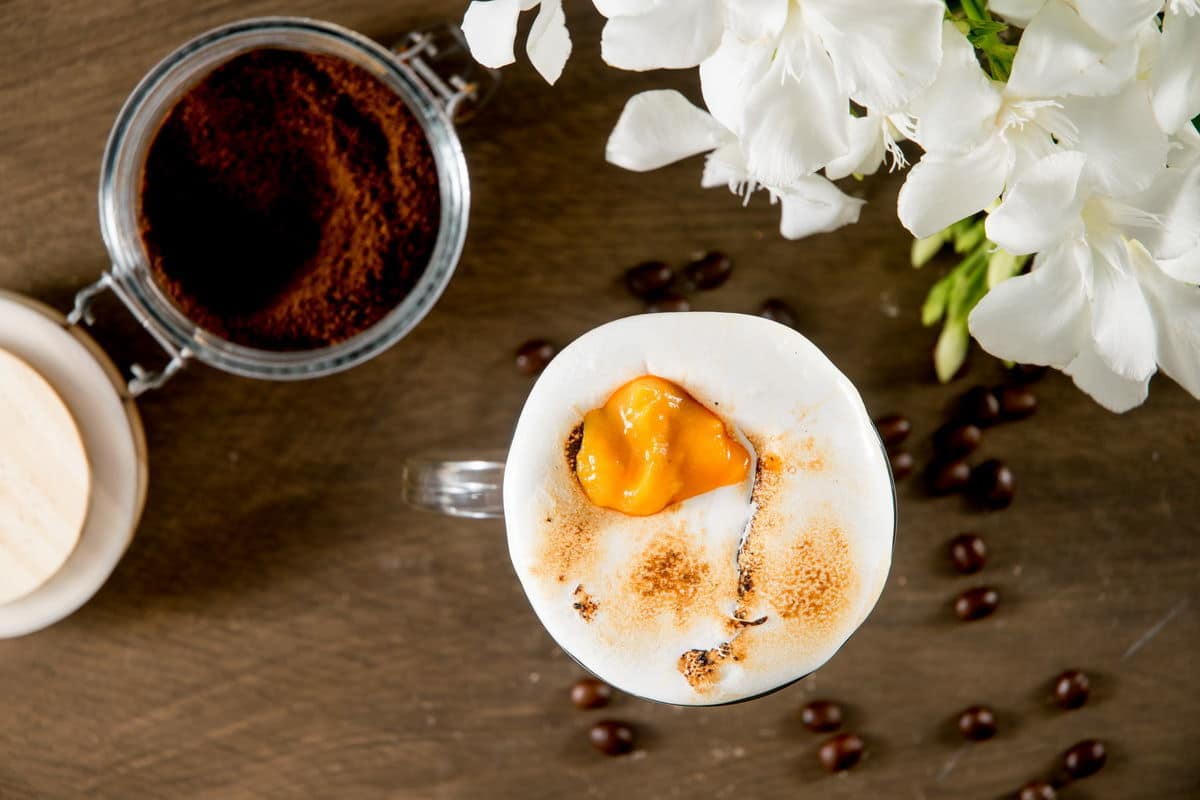 A cup of coffee and white flowers on a wooden table.