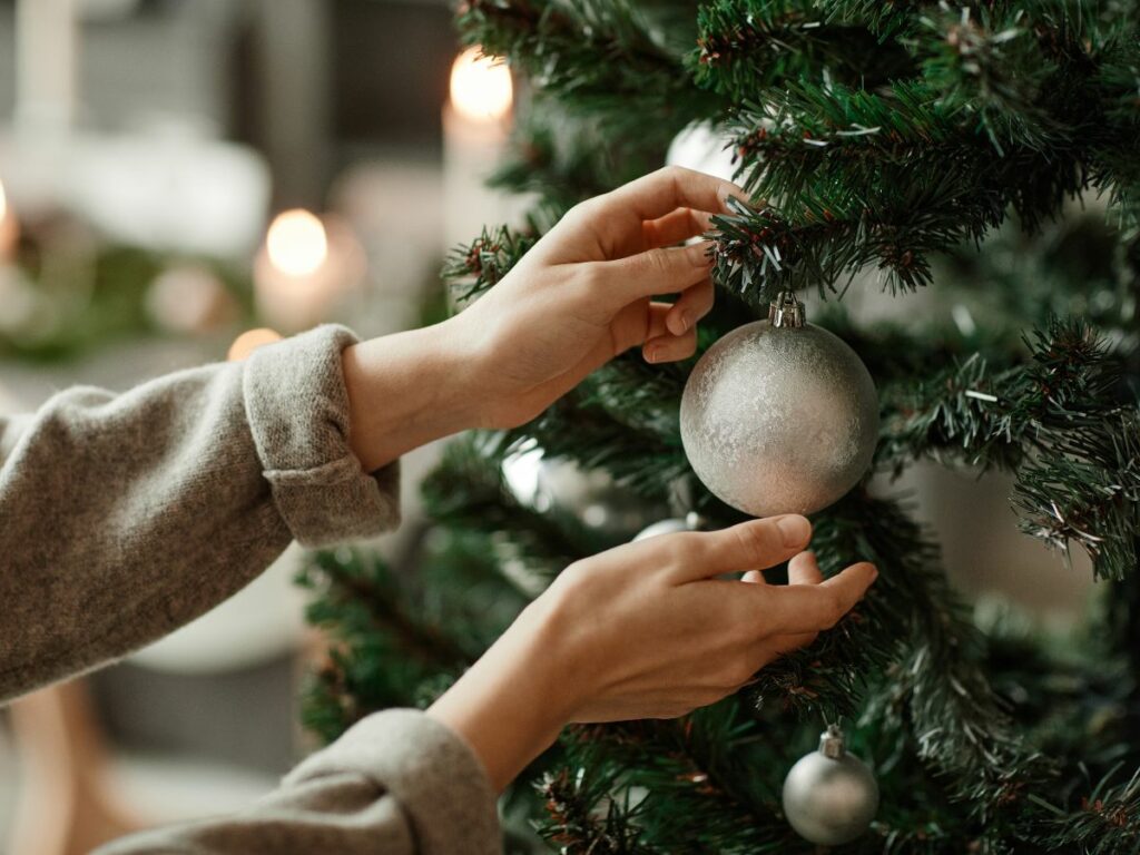 A pair of hands putting ornaments on a Christmas tree.