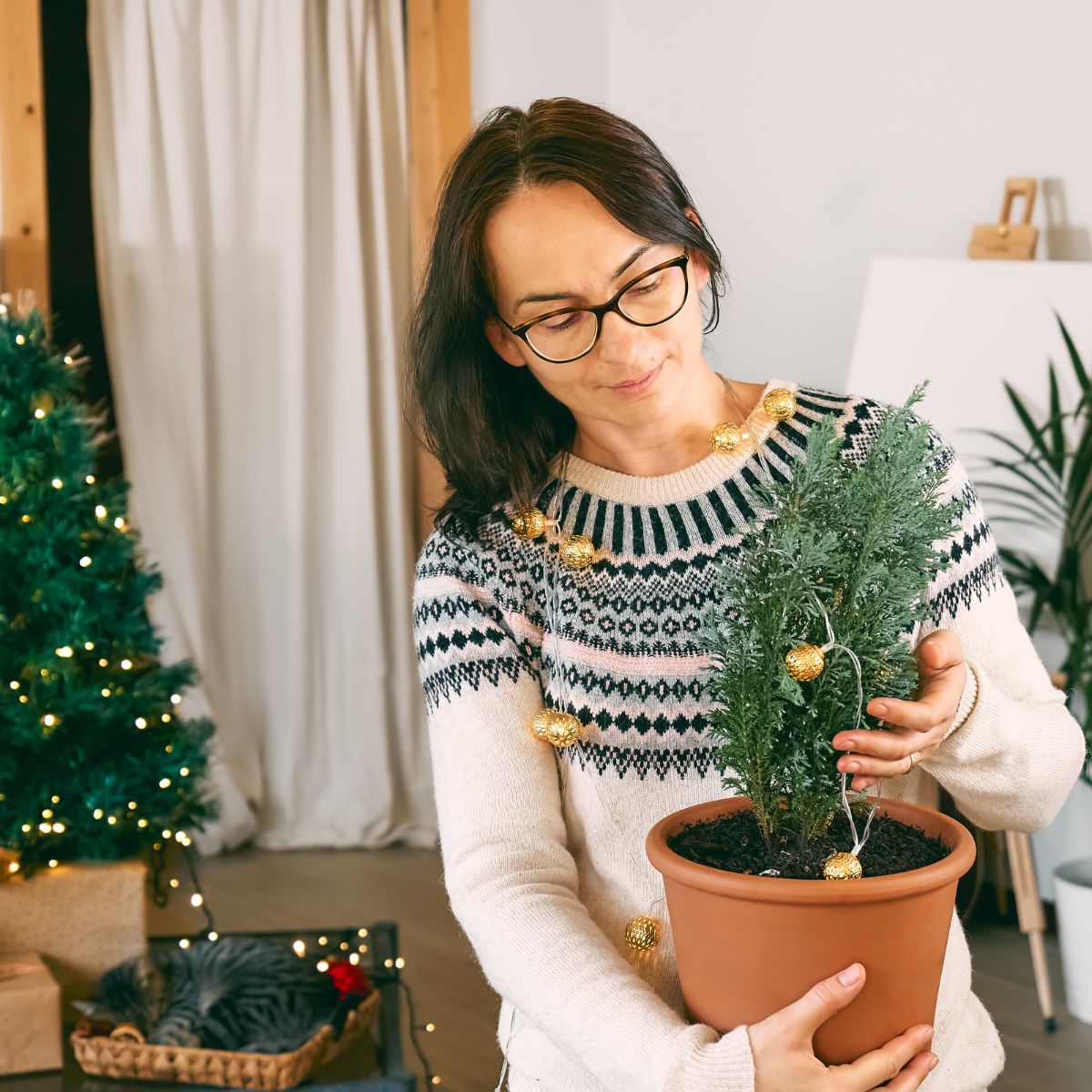 A woman decorating a potted christmas tree in her living room.