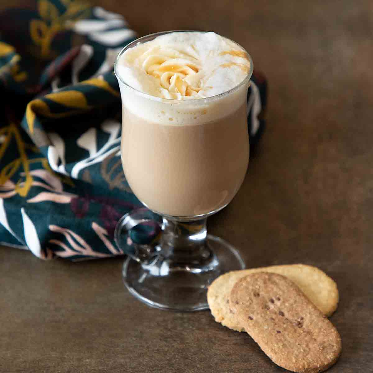 A latte with whipped cream next to cookies.