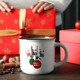 A woman is holding a christmas mug next to a gift.