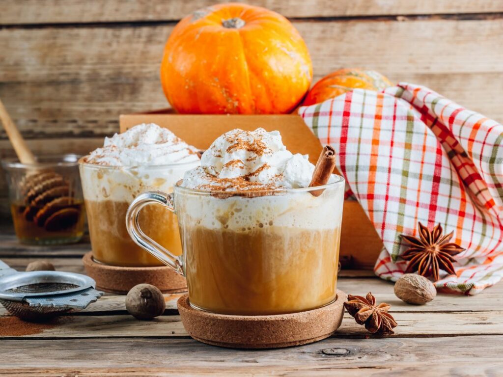Two mugs with whipped cream and pumpkins on a wooden table.