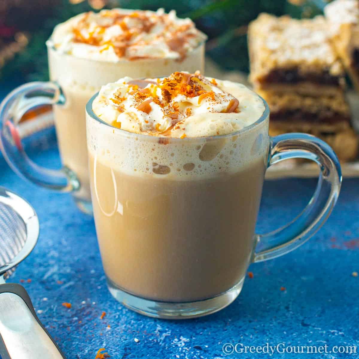 Two mugs of coffee with whipped cream and orange slices.