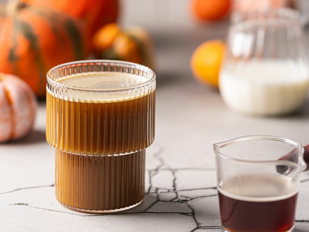 A glass of pumpkin spice latte next to a pumpkin.