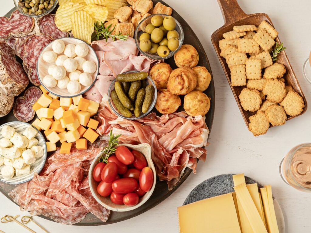 A round charcuterie platter of meats, cheeses and pickles with crackers on the side.