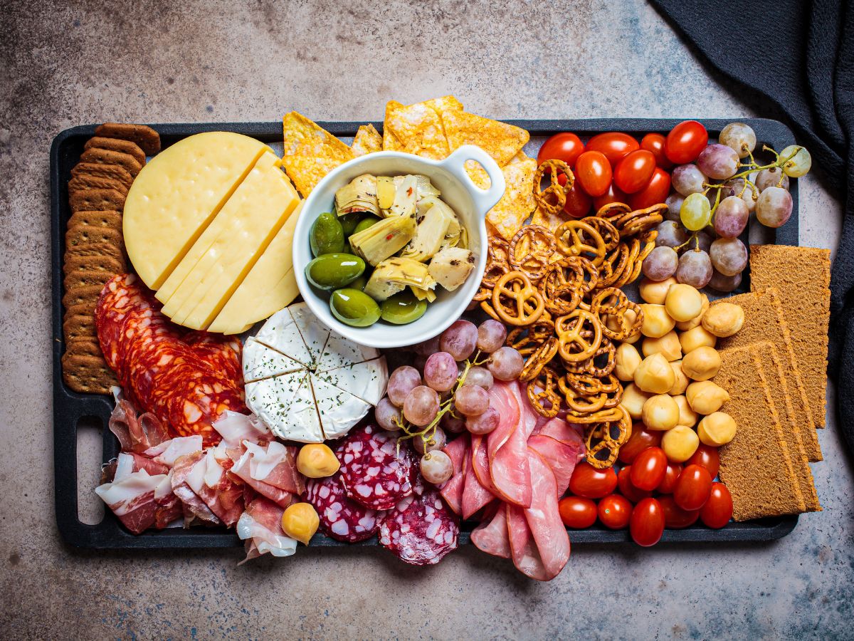 A tray full of meats, cheeses, snacks and crackers.